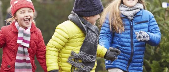 Three children running among Christmas trees with foster parents in the background - MumsNets